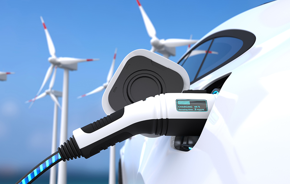 تصویر یک خودروی برقی در حال شارژ که در زمینه آن یک سری توربین‌های بادی قرار دارد که از منابع انرژی‌های تجدیدپذیر محسوب می‌شود.